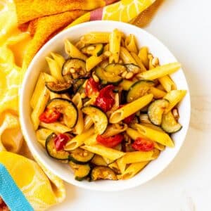Bowl of penne with tomatoes, zucchini, and pine nuts.